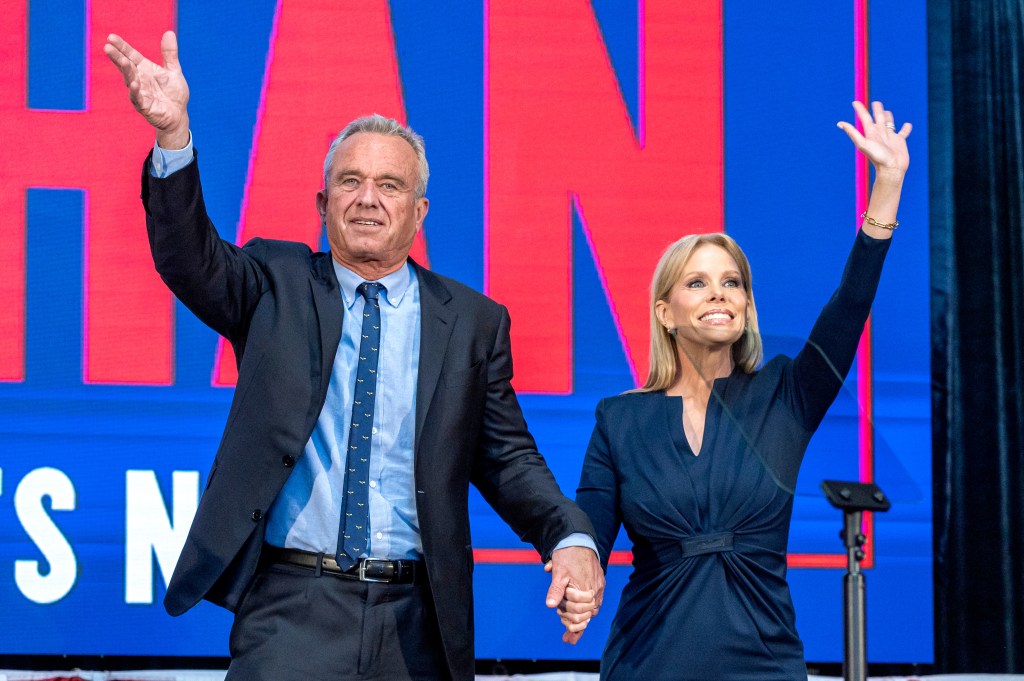 Robert F. Kennedy Jr. and wife Cheryl Hines raising their hands at a campaign event.