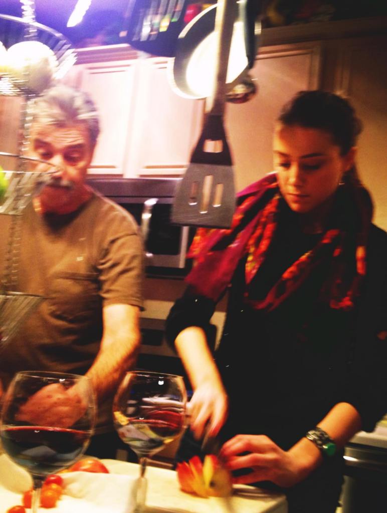 Amber Heard slicing an apple while a man stands beside her, with two glasses of red wine on the table.