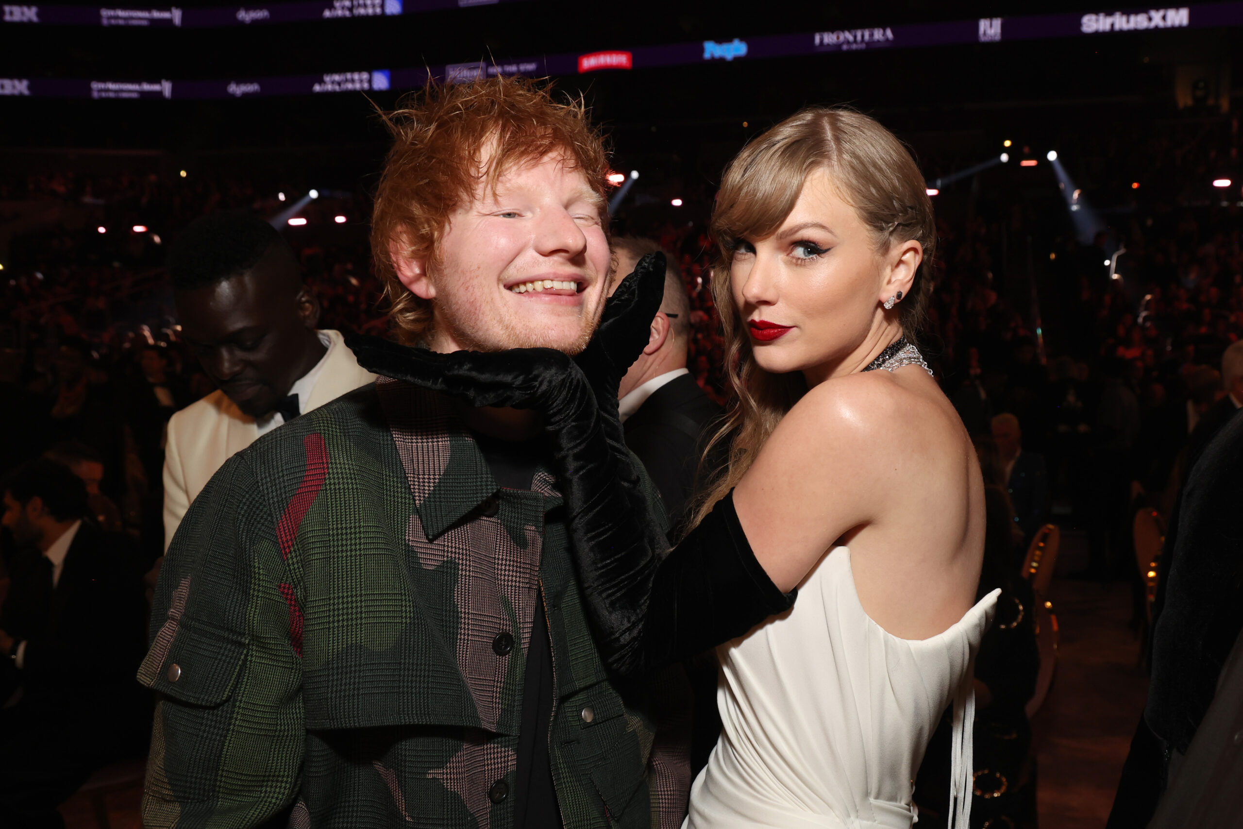 Taylor Swift gently lifting Ed Sheeran's chin with a black-gloved hand during a candid moment.