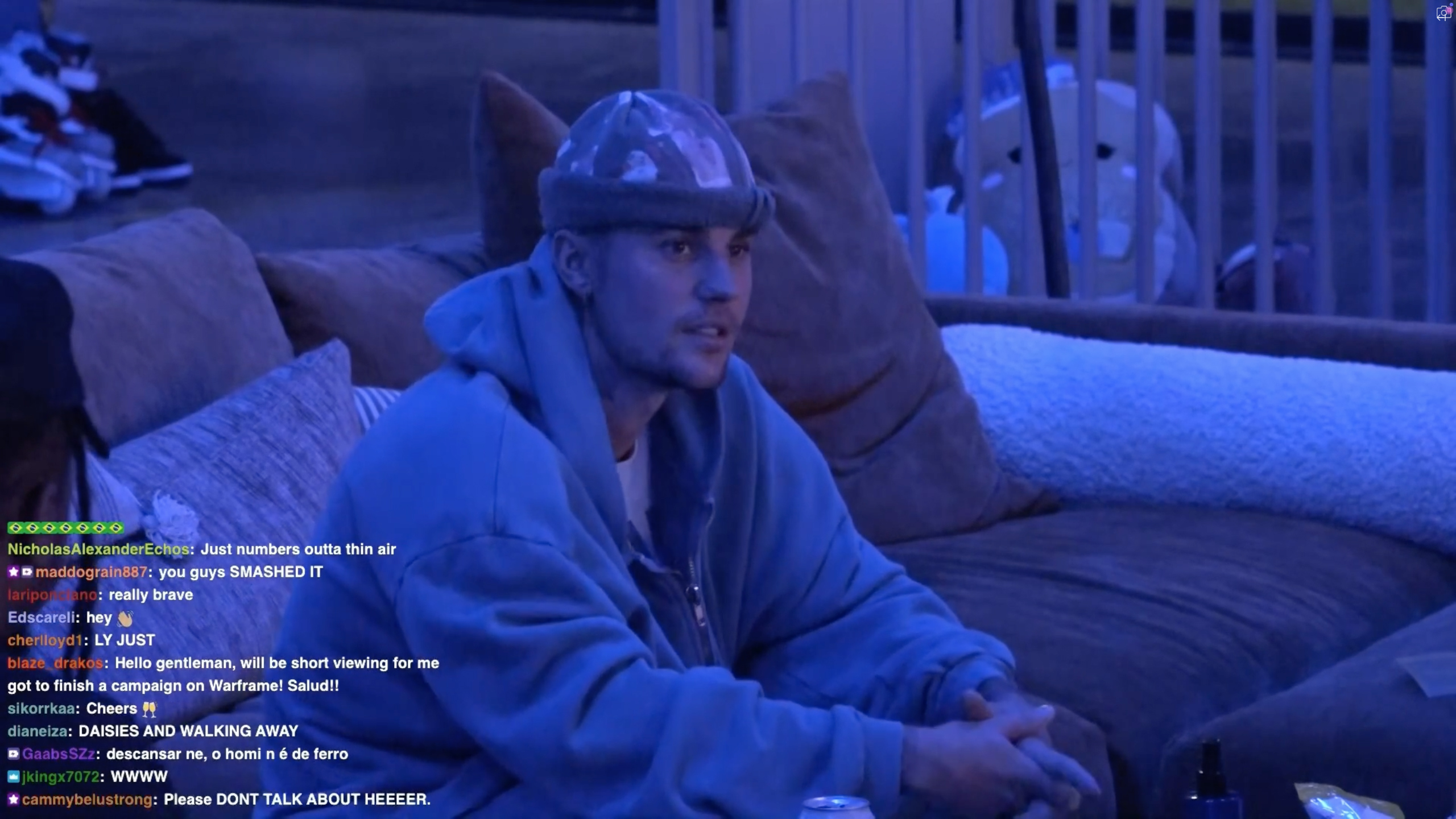 Justin Bieber in a blue hoodie and beanie on a couch during a Twitch livestream with chat comments visible.