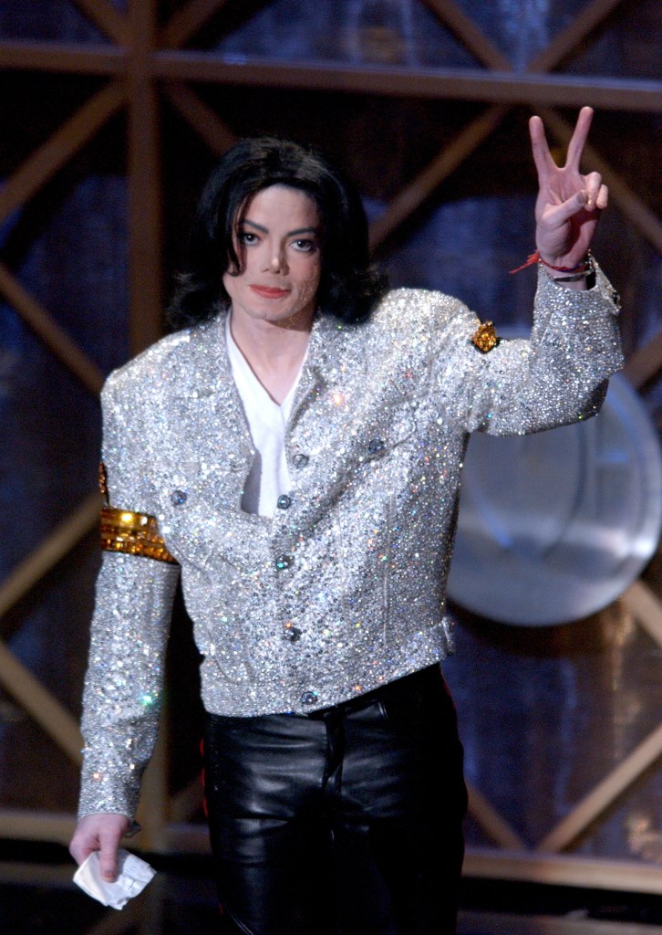 Michael Jackson performing on stage in a black outfit with gold accents.