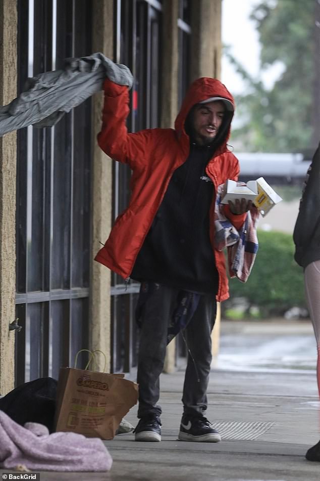 A passerby hands Tylor Chase a red raincoat during heavy Southern California storms