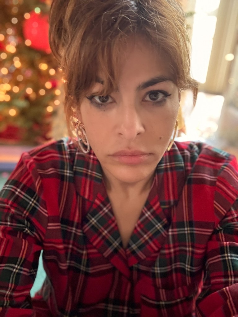 Eva Mendes wearing a red and green plaid shirt with a Christmas tree in the background.