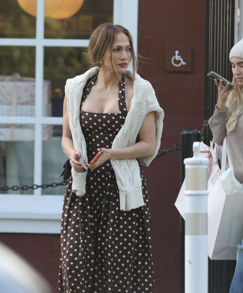 Jennifer Lopez in a brown polka-dot dress with a white knitted sweater draped over her shoulders.