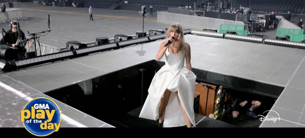 Taylor Swift in a white dress holding a microphone on stage, appearing emotional.