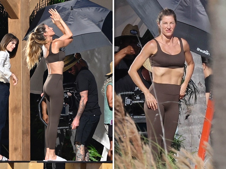 Gisele Bundchen filming a beach workout commercial in Miami, wearing a brown athletic set and stretching on the sand.