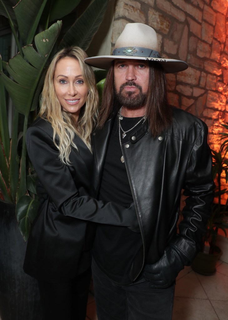 Tish Cyrus, in a black satin jacket, and Billy Ray Cyrus, in a black leather jacket and cowboy hat, pose for a photo.