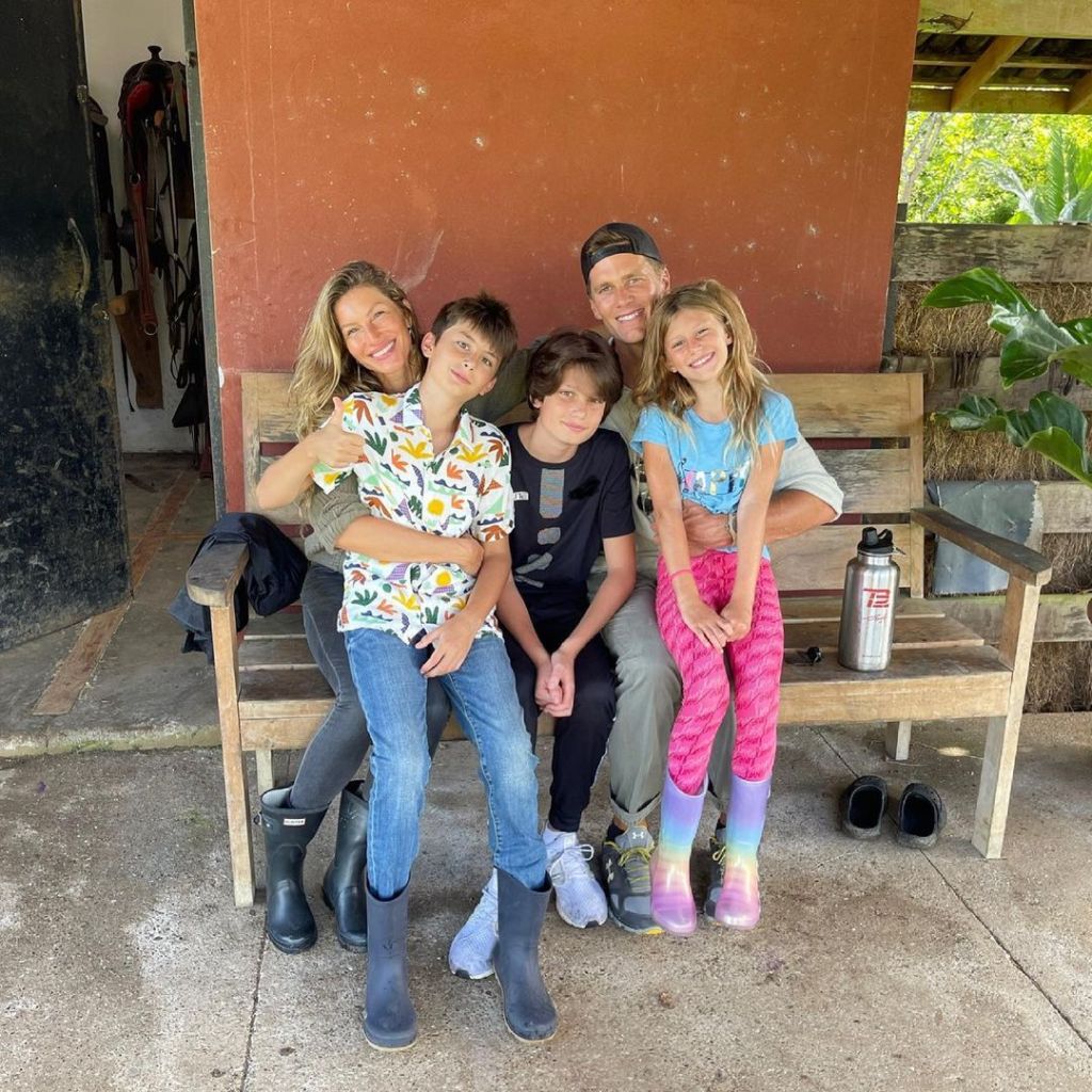 Gisele Bundchen and Tom Brady with their three children sitting together on a wooden bench.