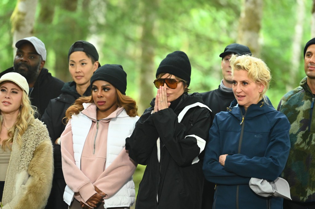 A group of reality show participants including Tara Lipinski, Ron Funches, Kristen Kish, Candiace Dillard Bassett, Lisa Rinna, and Dorinda Medley stand outdoors in a forest.