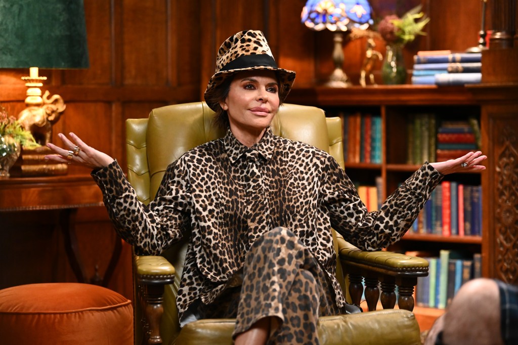 Lisa Rinna on The Traitors in a leopard-print hat and outfit, seated in a green leather armchair.