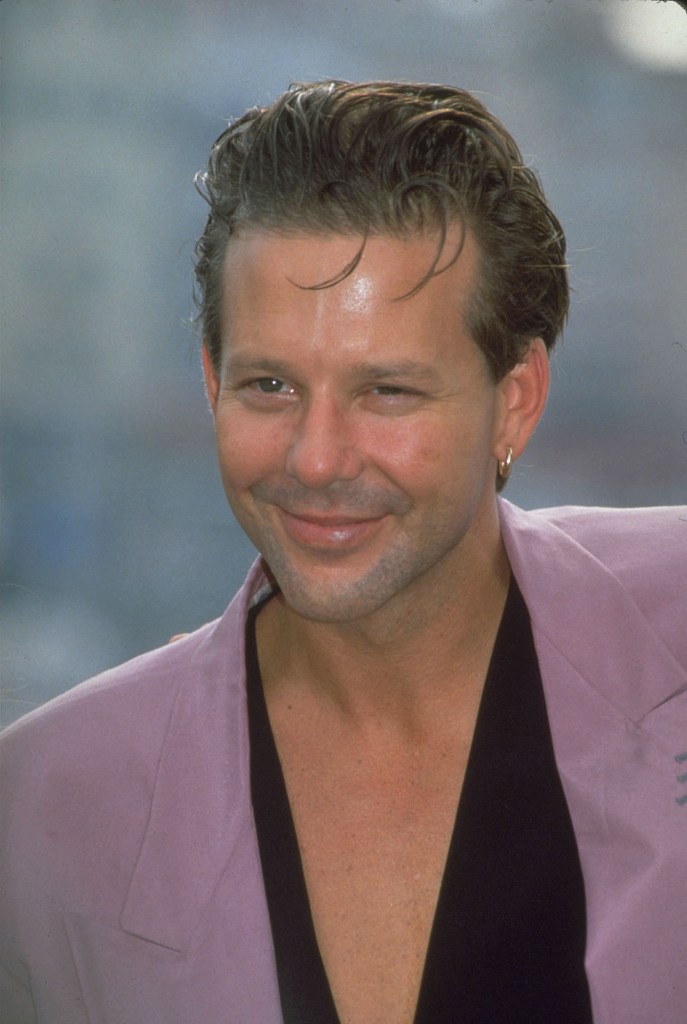 Actor Mickey Rourke in a light purple jacket and black v-neck shirt.