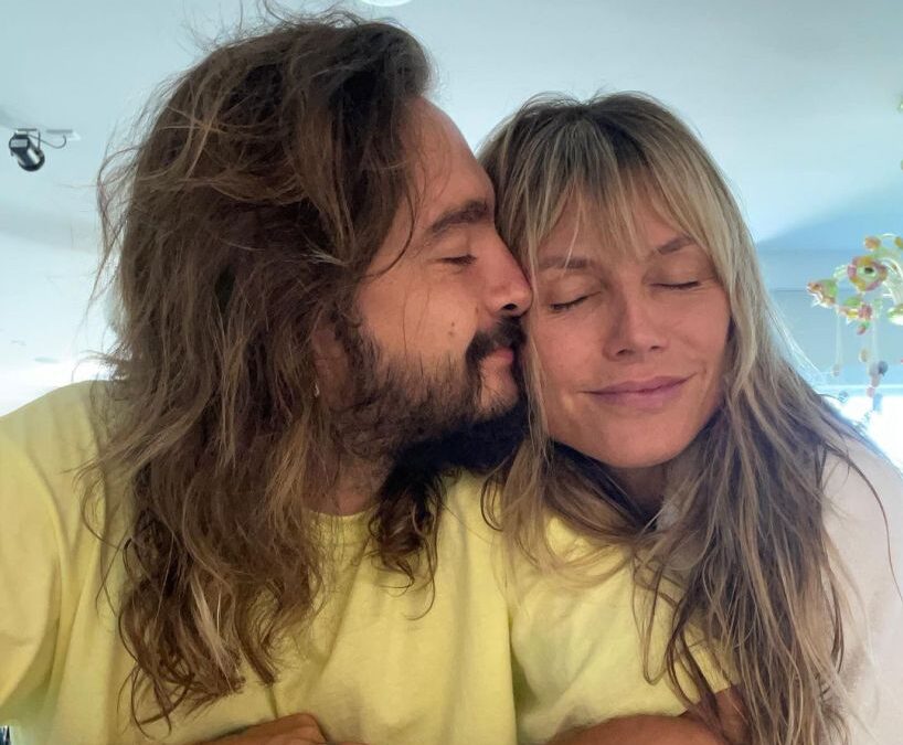 Heidi Klum and husband Tom Kaulitz cuddle at a table with plates of food and drinks.