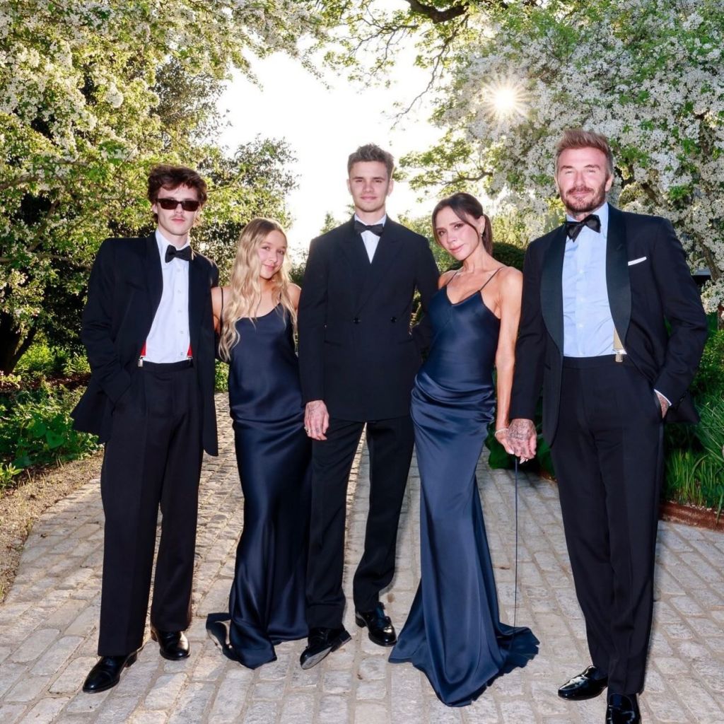 David and Victoria Beckham with their children, Cruz, Harper, and Romeo, in formal attire on a paved path outdoors.