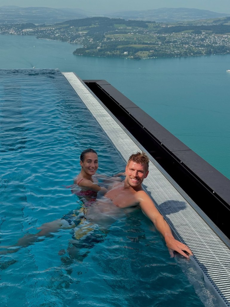 Amanda Batula and Kyle Cooke in an infinity pool with a lake and mountains in the background.