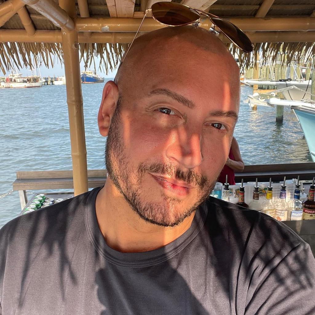 Jasen Kaplan smiling with sunglasses perched on his head near a marina.