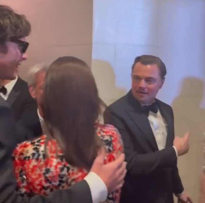 Melissa Elordi turns back toward Sean Penn as Leonardo DiCaprio gestures to introduce his mother backstage at the Golden Globes.
