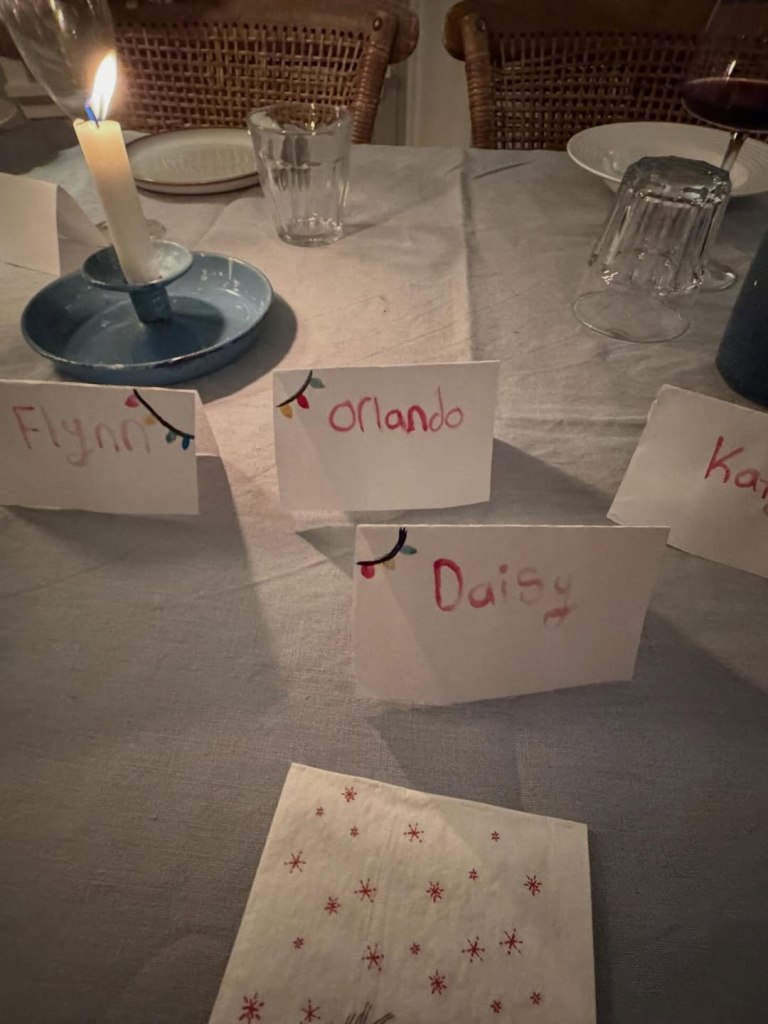 Christmas-themed place cards for Flynn, Orlando, and Daisy set at a dinner table with a lit candle.