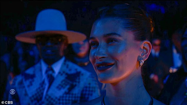 Hailey Bieber smiles and cheers in the audience during Justin Bieber's Grammys performance.