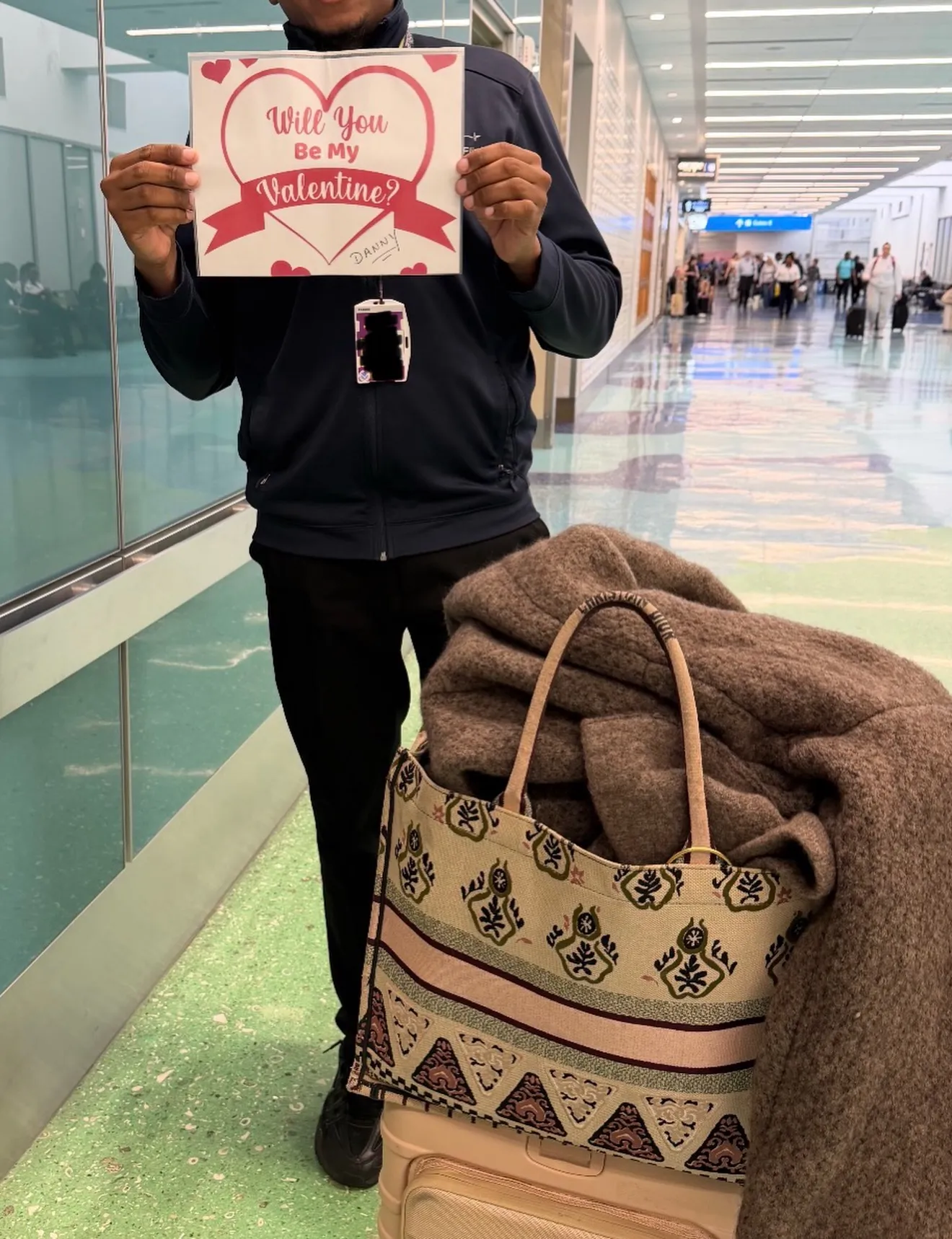 A person holding a Valentine's card with "Will You Be My Valentine?" written on it.