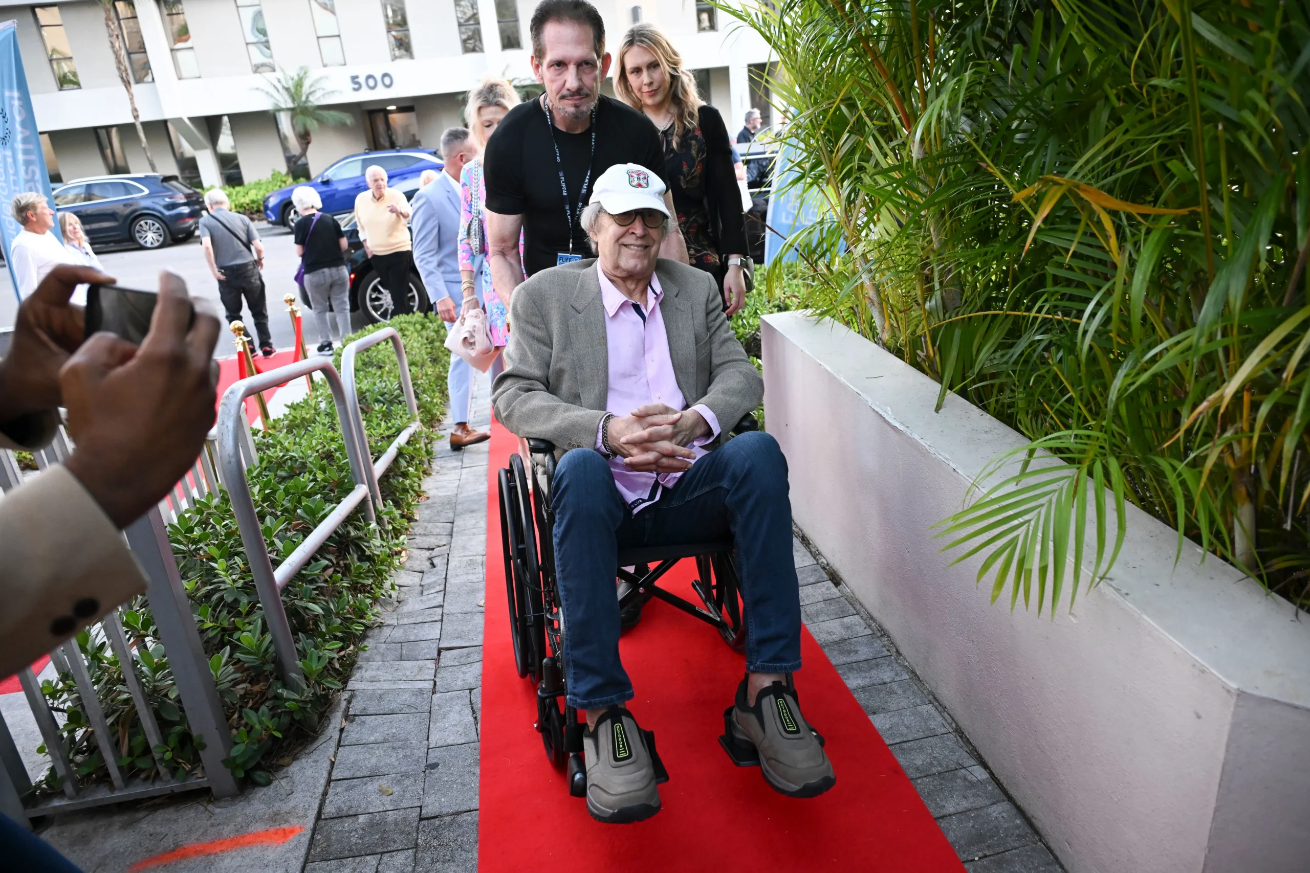 Chevy Chase arrives in a wheelchair on the red carpet at Savor Cinema.