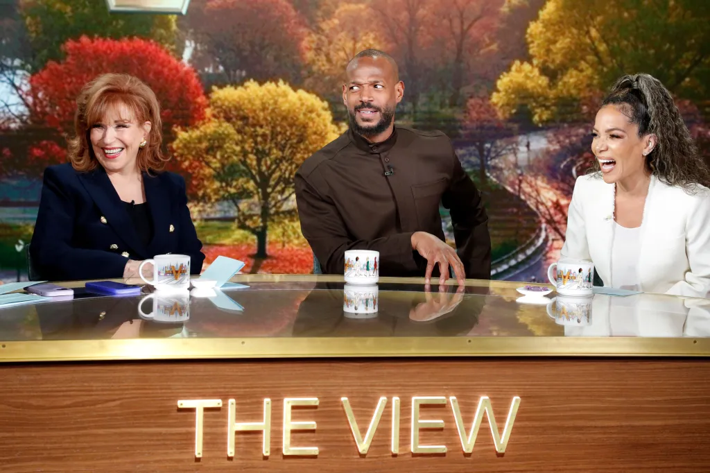 The cast of The View and guest Marlon Wayans sit behind a crescent-shaped desk.