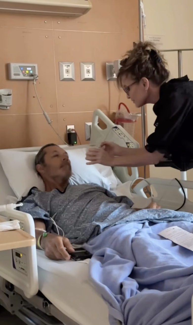 Sarah Palin sits beside Ron Duguay in a hospital room