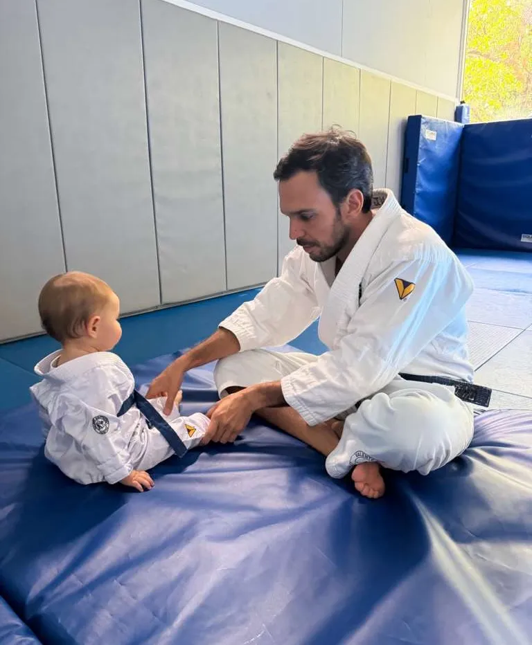 A man in a gi adjusts a baby's gi on training mats in a photo shared on Gisele's Instagram.