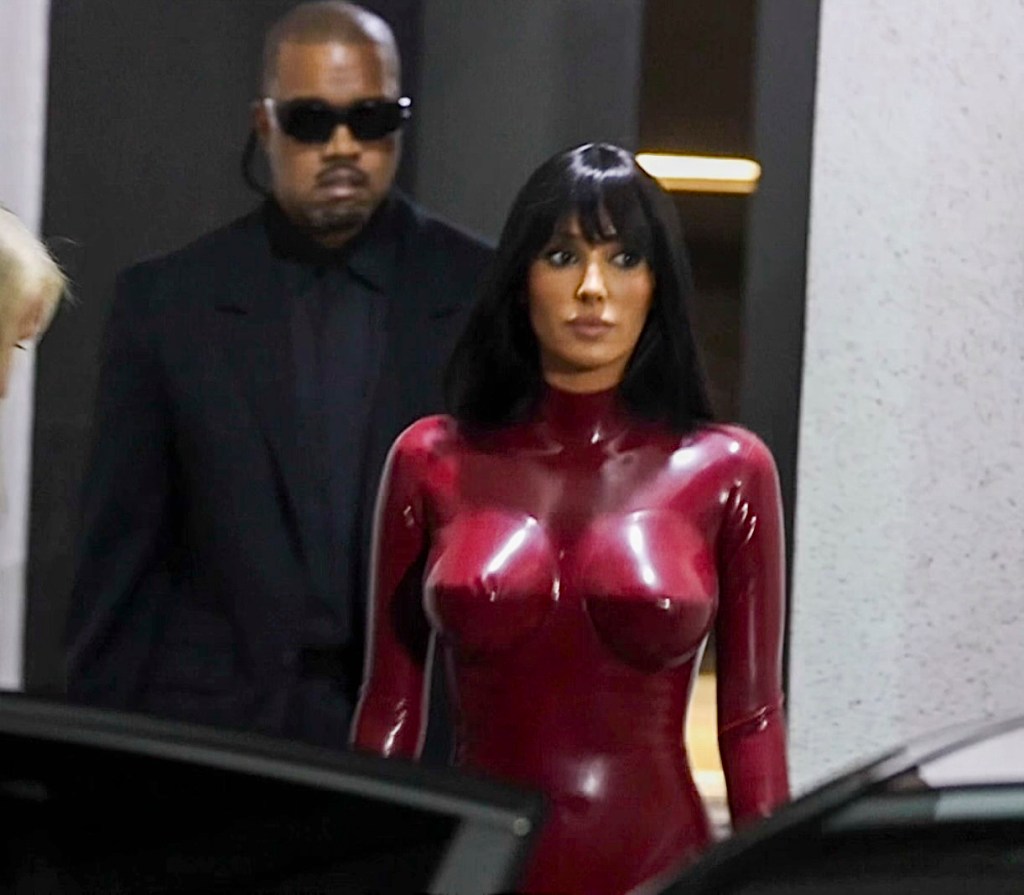 Bianca Censori in a red bodysuit with Kanye West in a black suit and sunglasses.