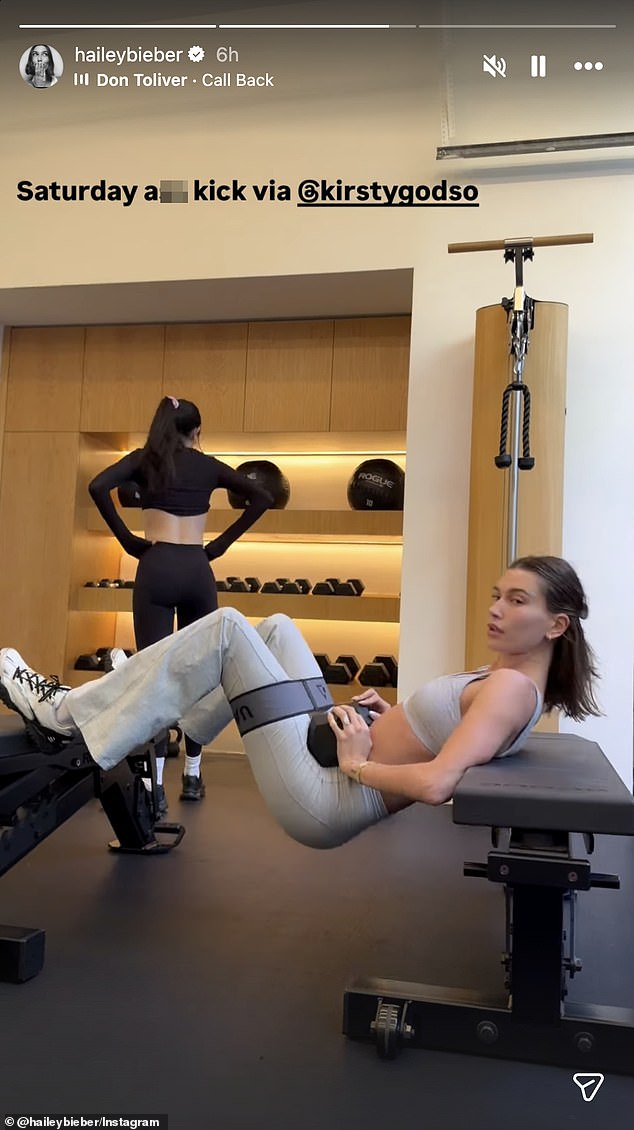 Hailey Bieber performs dumbbell hip thrusts across two benches in a gym with trainer Kirsty Godso (Instagram Story, Mar 8, 2026).