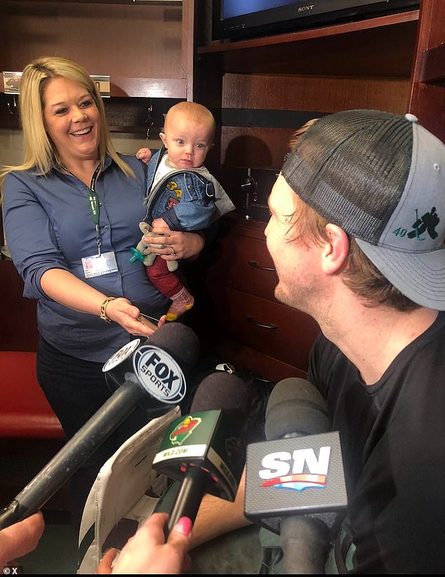 Jessi Pierce holds her baby while interviewing a Minnesota Wild player in the locker room.