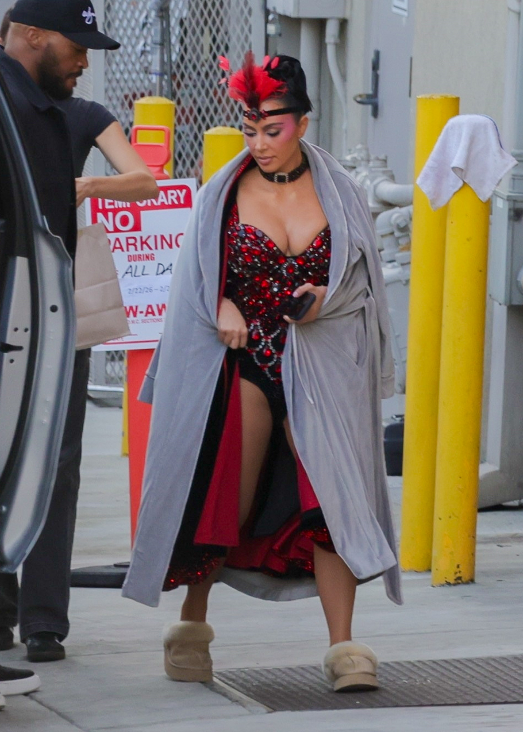 Kim Kardashian in showgirl costume under a gray bathrobe with Ugg-style slippers while moving around The Fifth Wheel set.