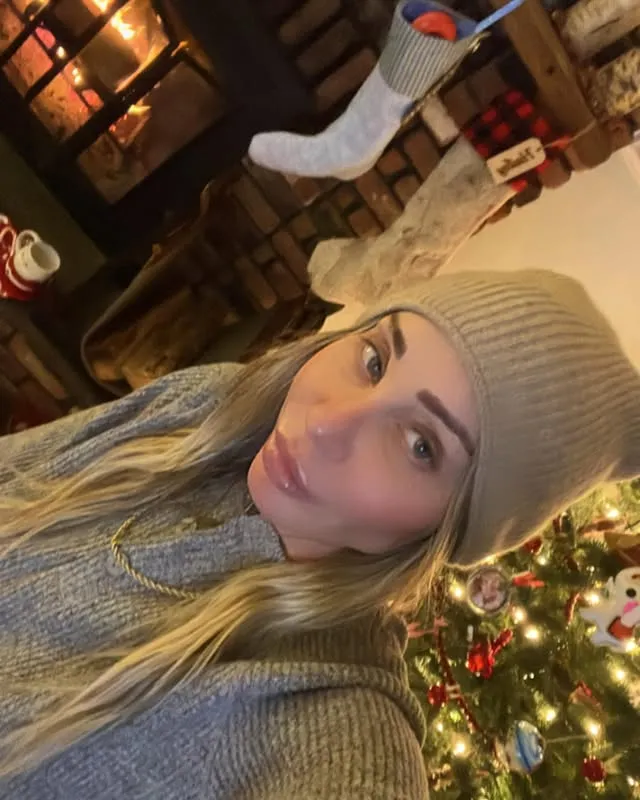 Hailey Glassman takes a selfie in front of a fireplace and Christmas tree.