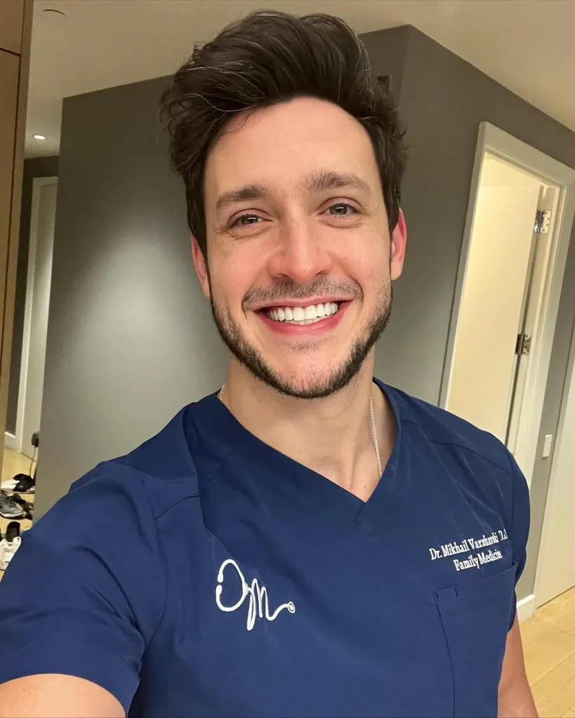 Portrait of Dr. Mikhail Varshavski, a family medicine doctor, smiling in blue scrubs.