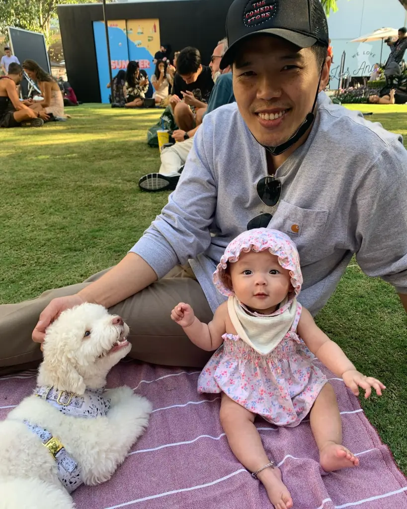Alex Duong sitting on a picnic blanket with his daughter Everest and a white poodle in 2021.