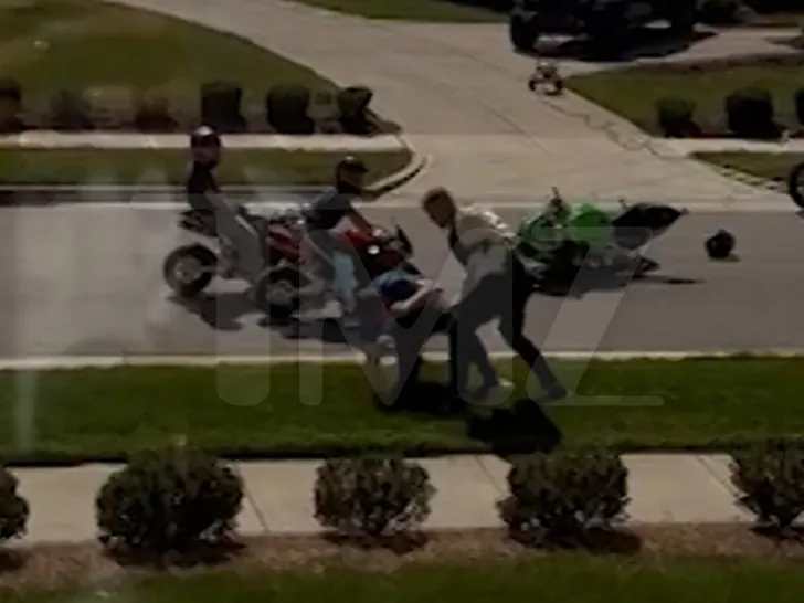 Smartphone video still reportedly showing Alan Ritchson and a neighbor grappling on a suburban street while two minors on minibikes are nearby.