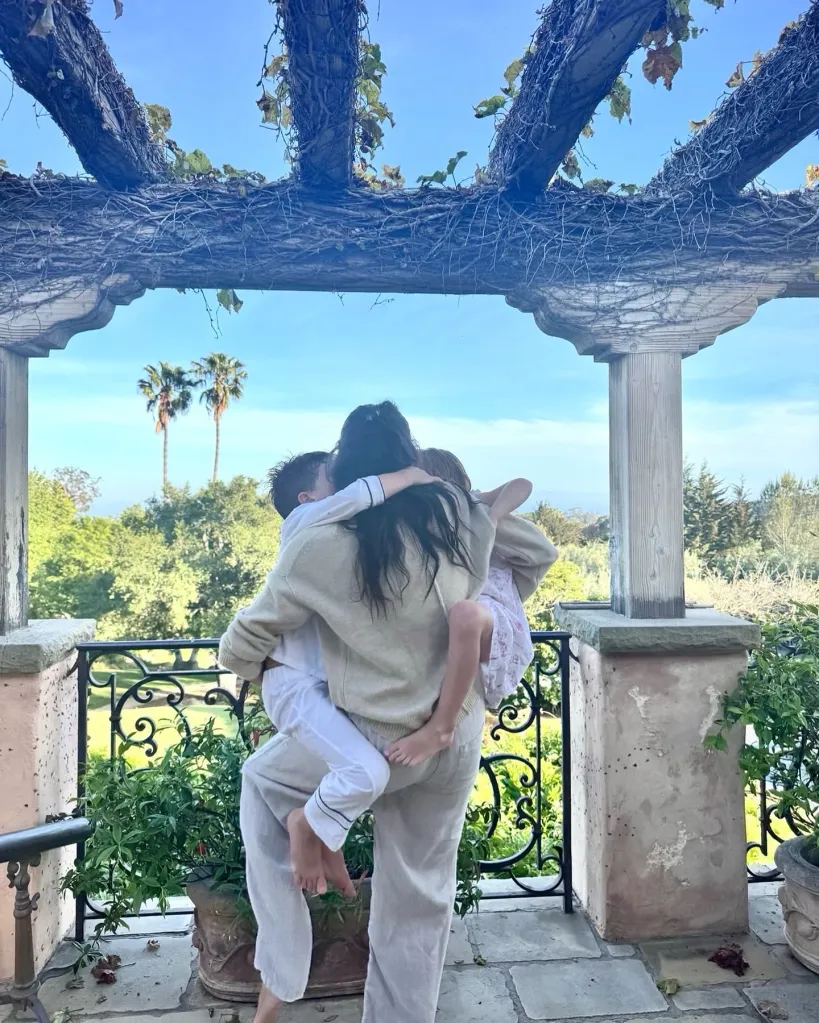 Meghan Markle holding Archie and Lilibet on a balcony under a blue sky.