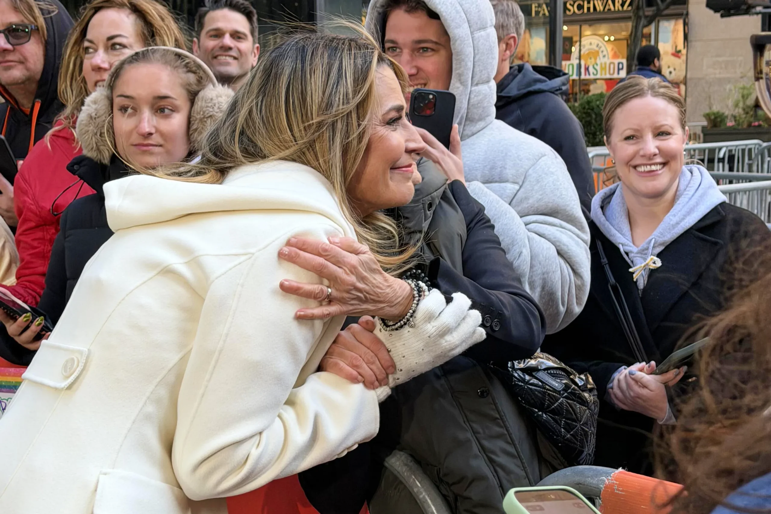 Savannah Guthrie tears up while hugging a fan outside NBC's Rockefeller Center as supporters hold signs.