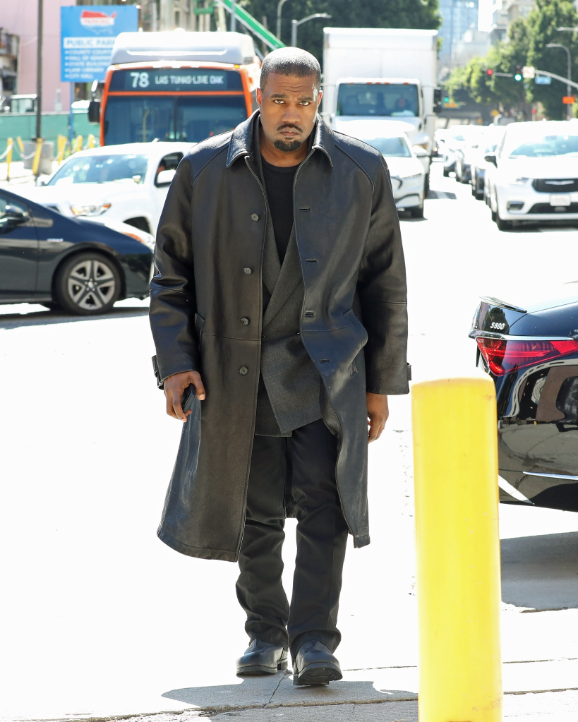 Kanye West walking in Los Angeles wearing a long black leather coat.