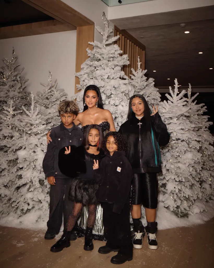 Kim Kardashian with her children in a holiday photo in front of snowy Christmas trees.