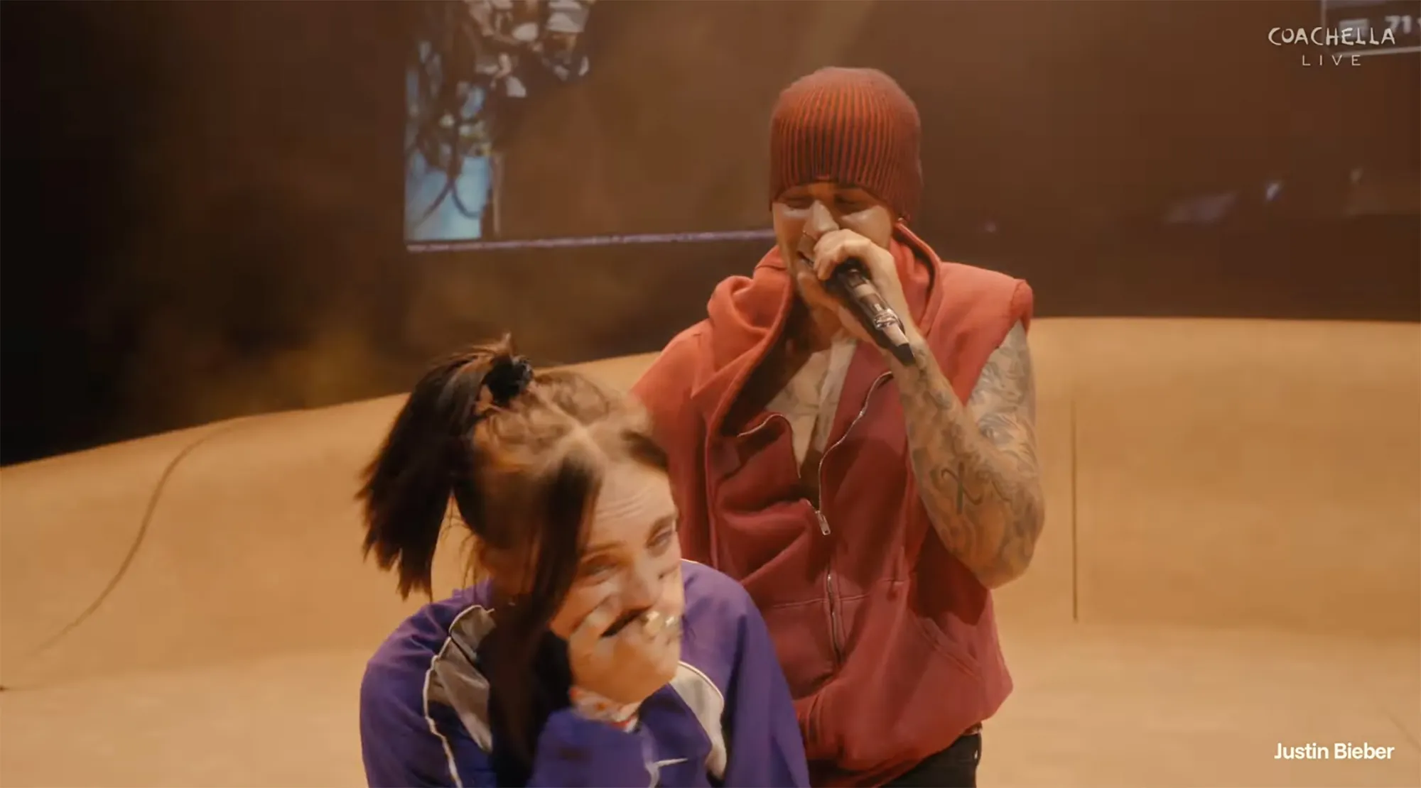 Justin Bieber wraps an arm around Billie Eilish while serenading her with One Less Lonely Girl at Coachella 2026.